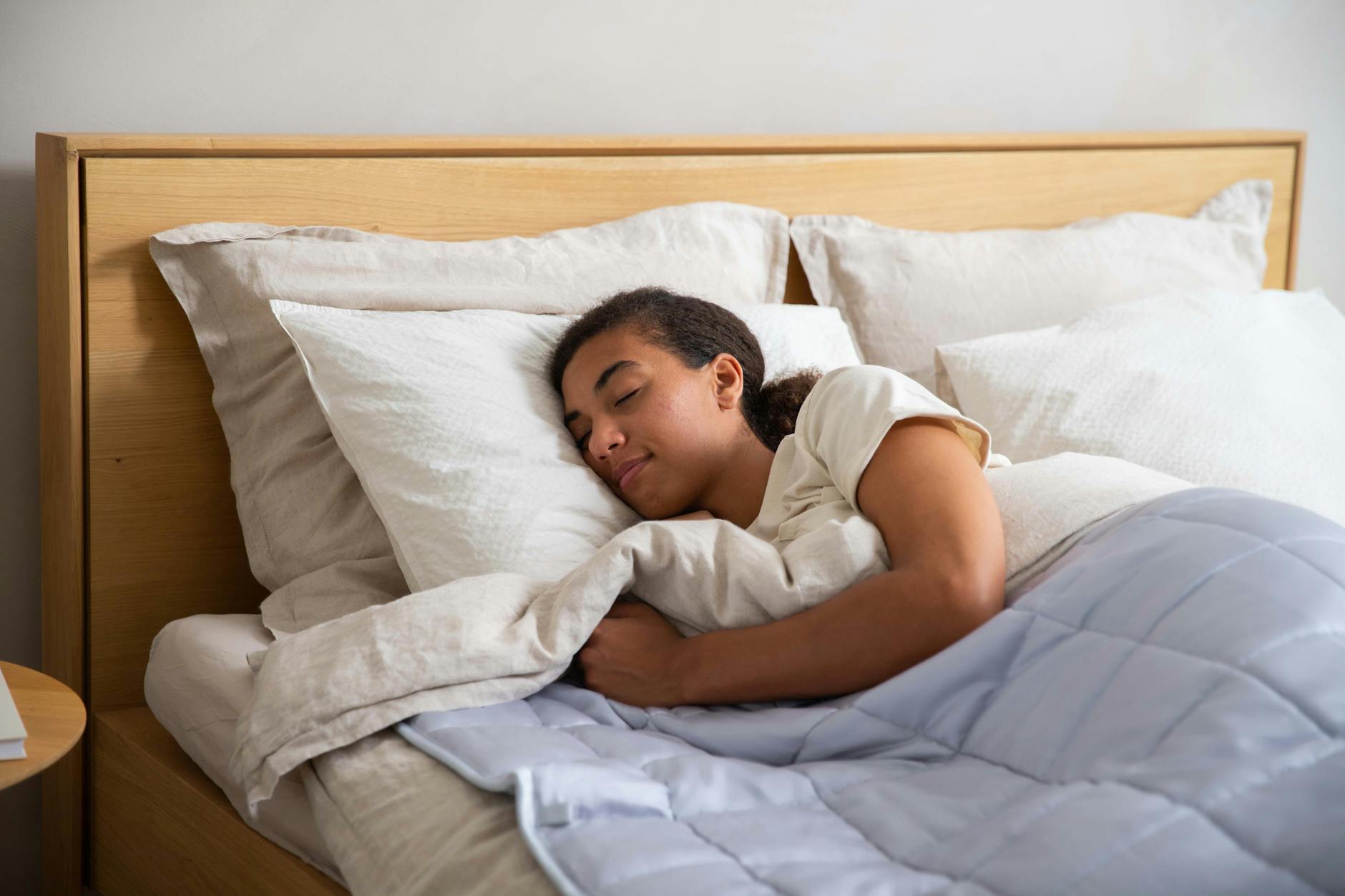 A person asleep on their side in a bed with pale linen bedding and a light blue quilt