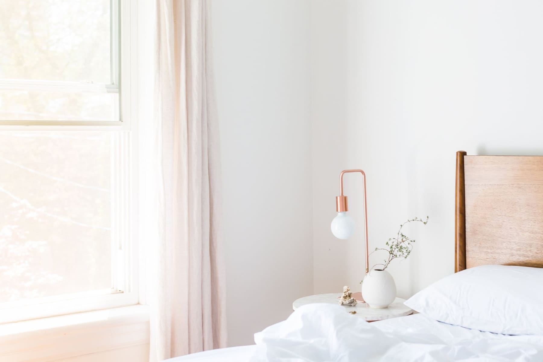 A bright, calm bedroom with white bedding and a window
